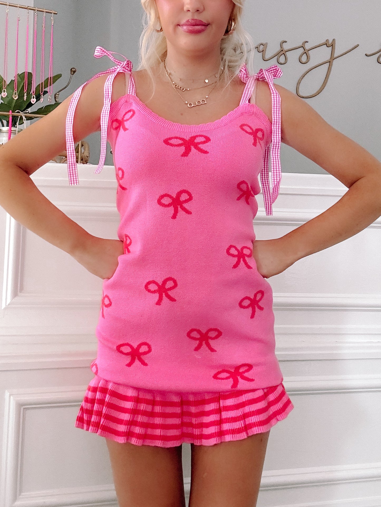 Hot pink knit dress with red bow pattern, gingham straps, and pleated hem.