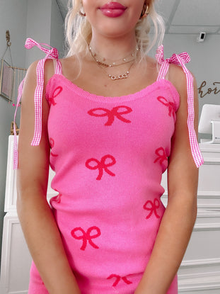 Hot pink knit dress with red bow pattern and gingham ribbon straps.