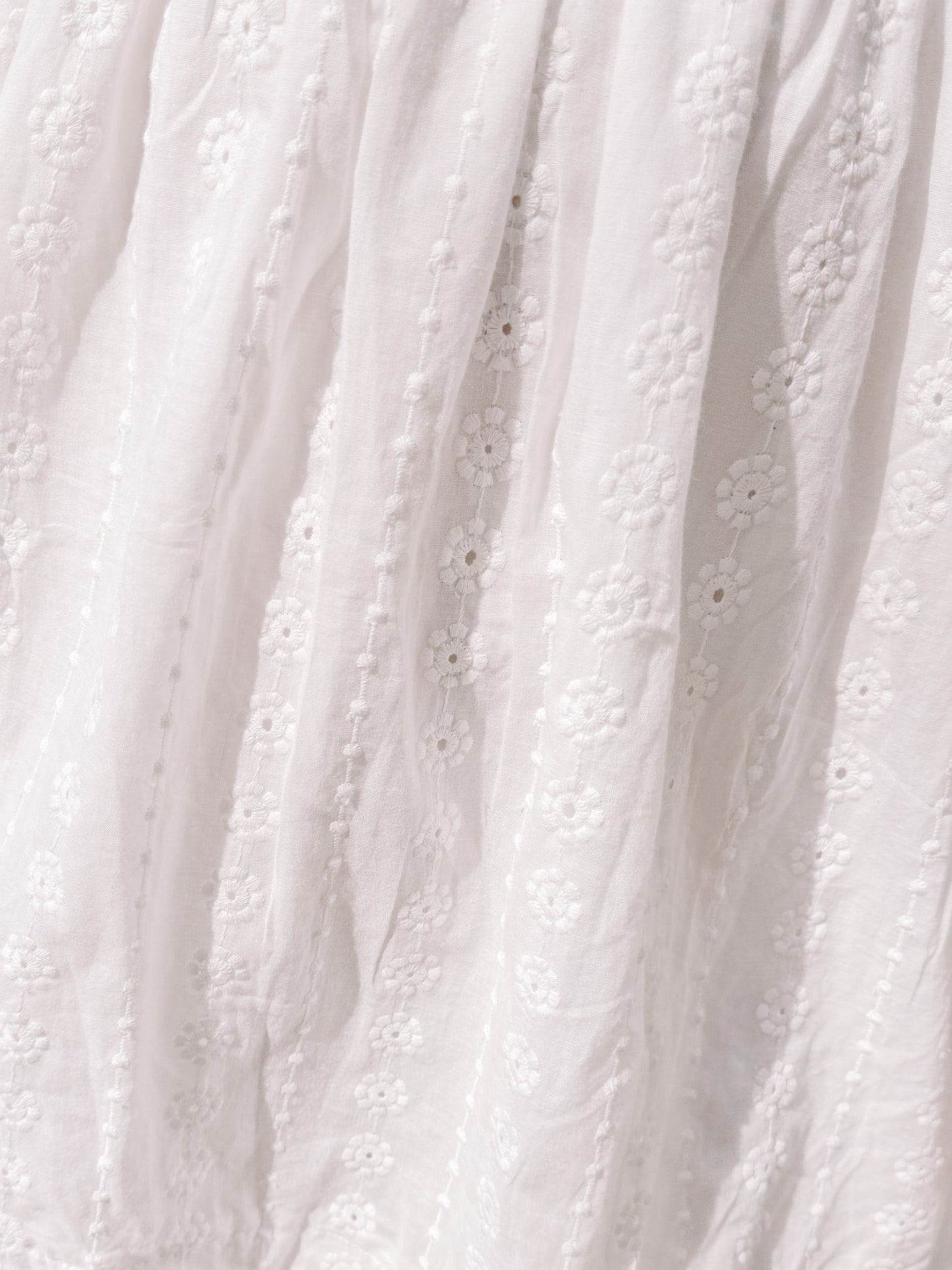 White eyelet dress fabric detail; delicate floral embroidery.