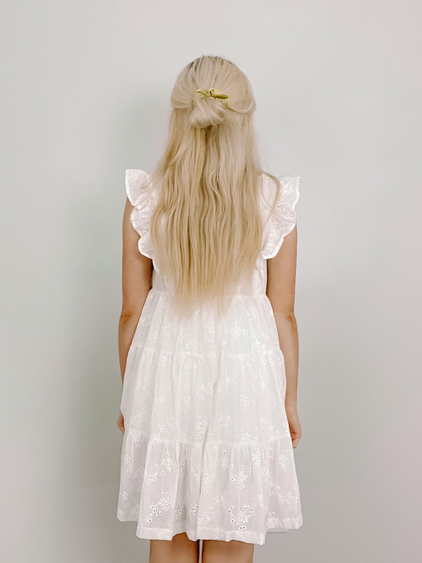 White eyelet dress, tiered skirt, rear view against a light background.