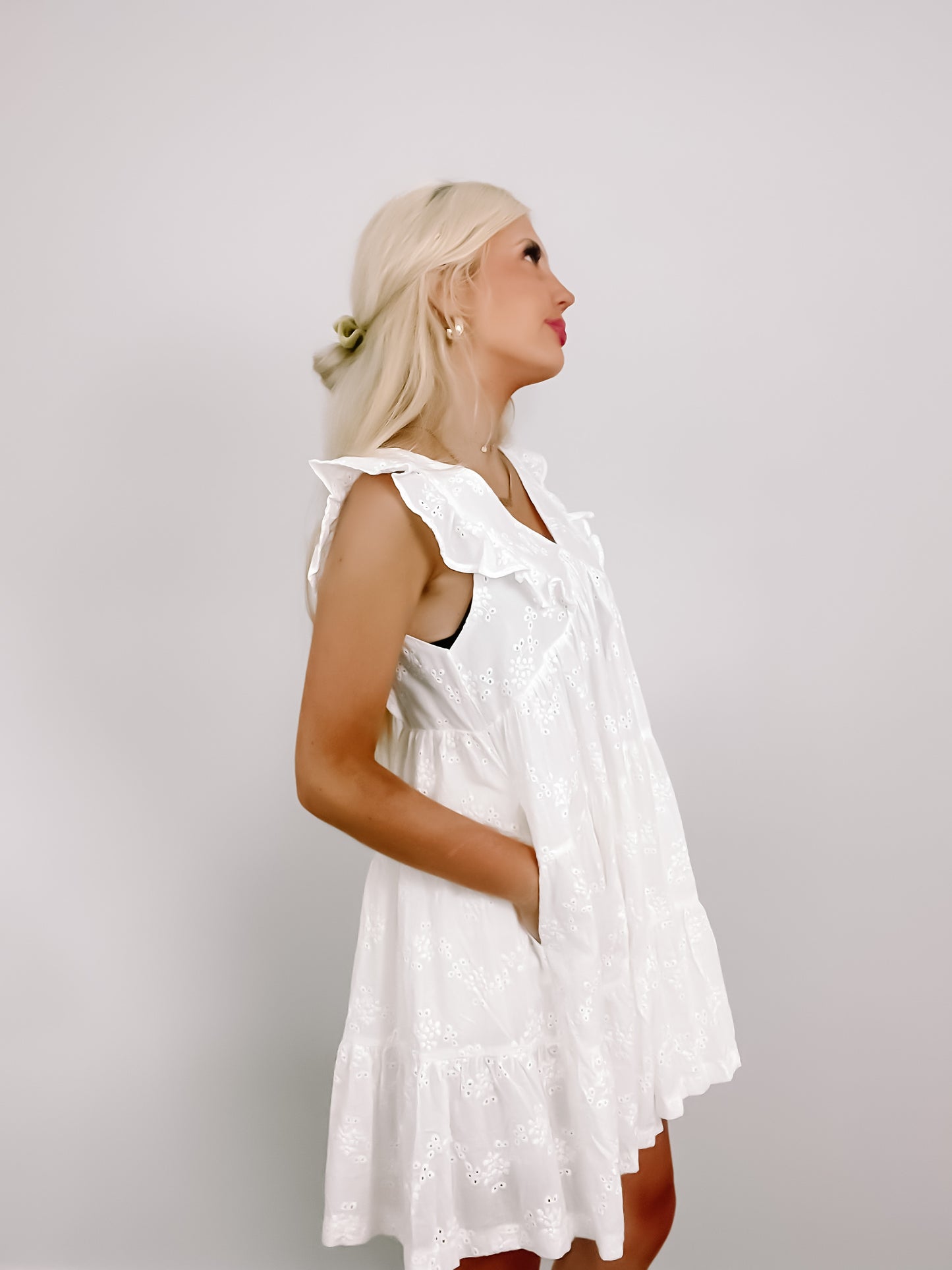 White eyelet mini dress with ruffled details, shown on a model against a neutral backdrop.