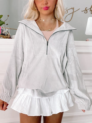 Grey corduroy zip-up jacket styled with a white ruffle skirt.