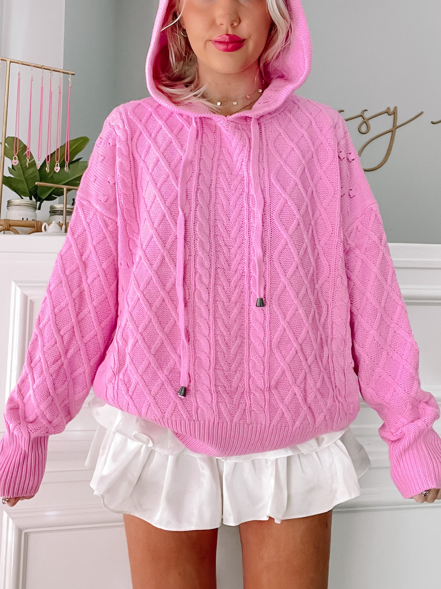 Pink cable knit hoodie sweater with drawstring, styled with a white ruffled skirt.