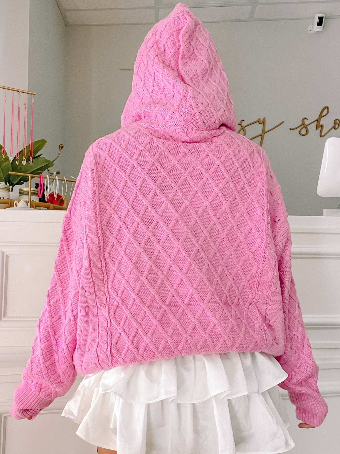 Pink cable-knit hoodie sweater, oversized fit, shown from the back with a white ruffle skirt.