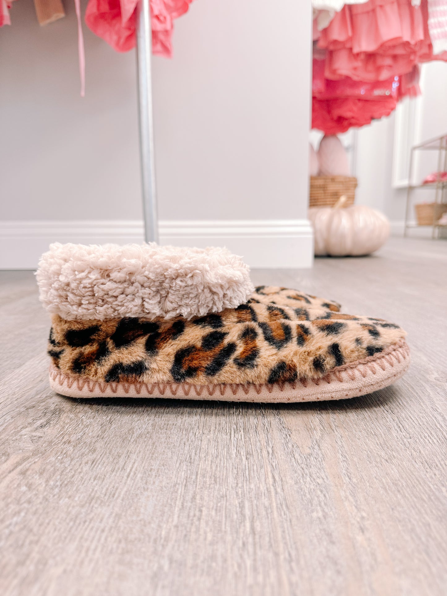 Leopard print fuzzy slippers with a cream sherpa lining, resting on a wood floor.
