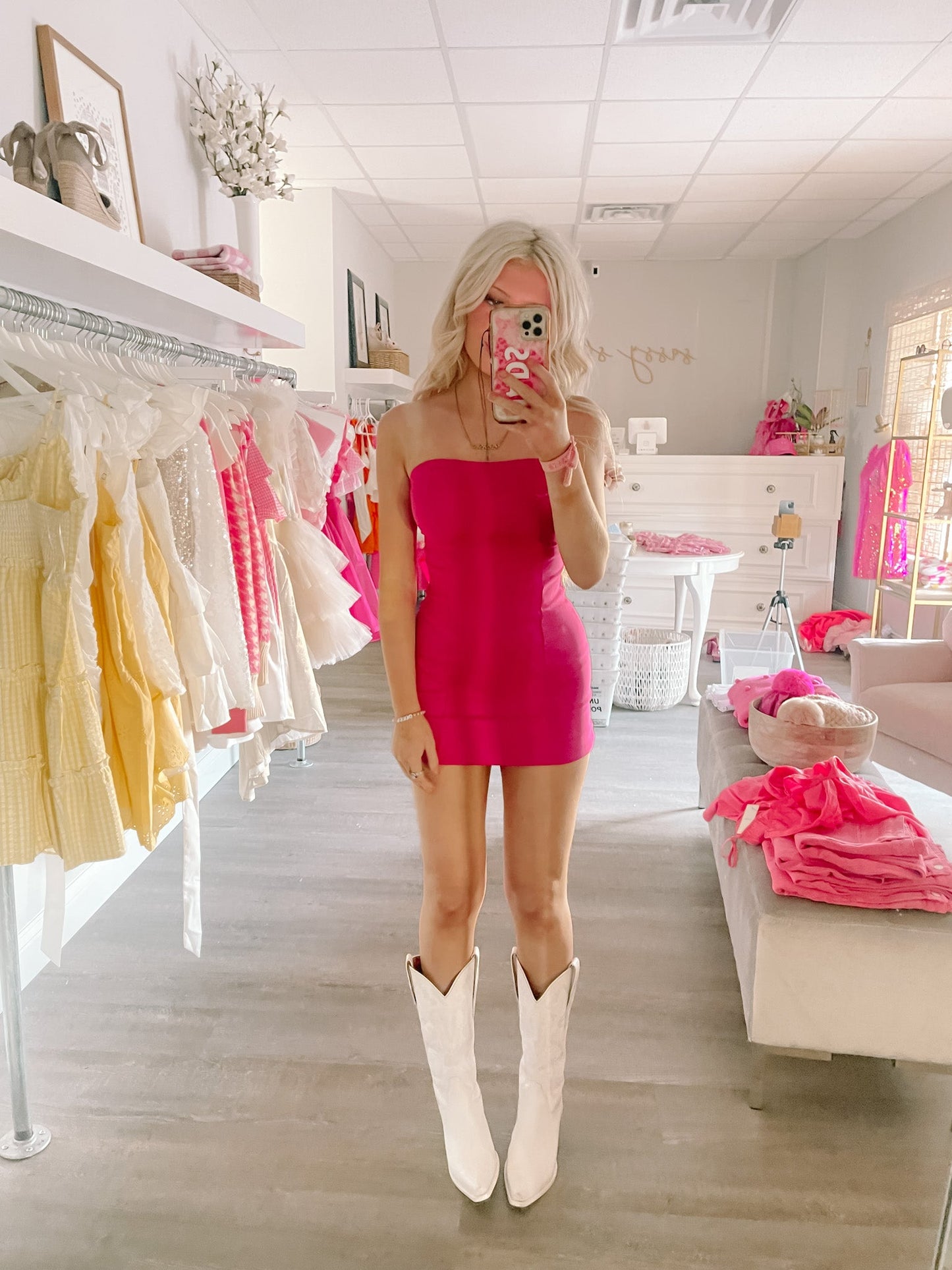 Hot pink mini dress, strapless neckline, styled with white cowboy boots in a bright boutique.