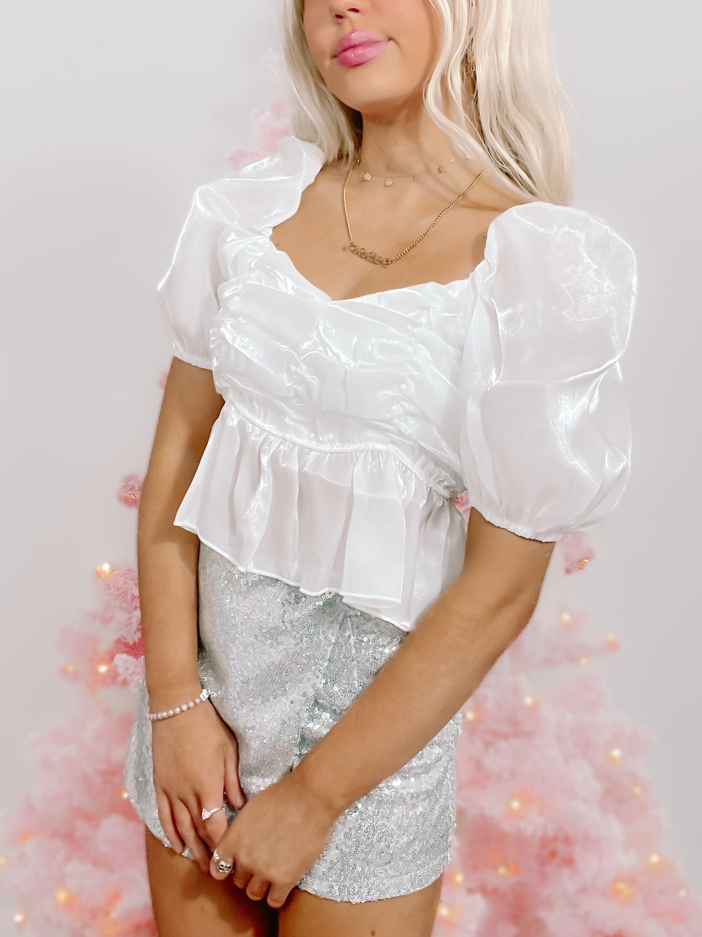 White puff-sleeve crop top with a ruffled hem, modeled against a pink Christmas tree.