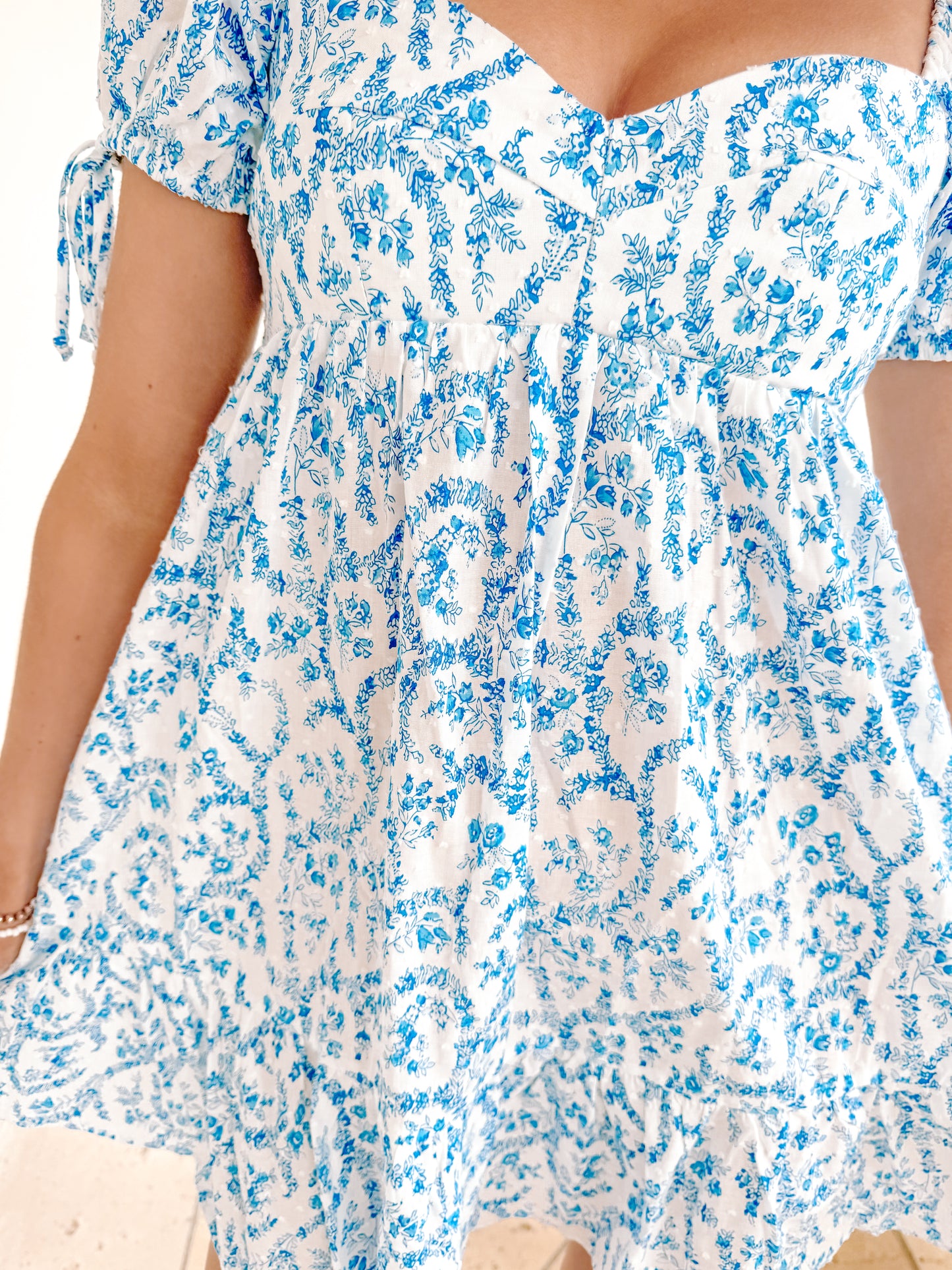 White eyelet mini dress with blue floral print, puff sleeves and tie detail.