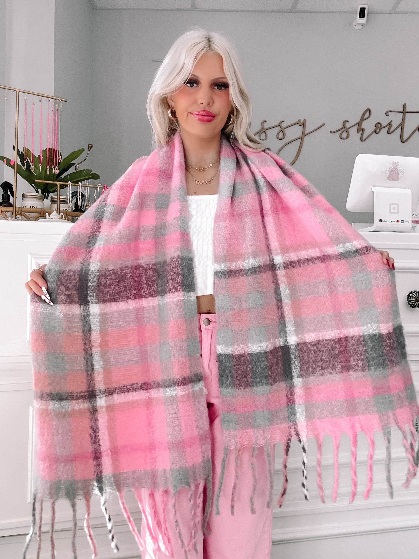 Pink and gray plaid scarf with fringed edges, styled over a white top.
