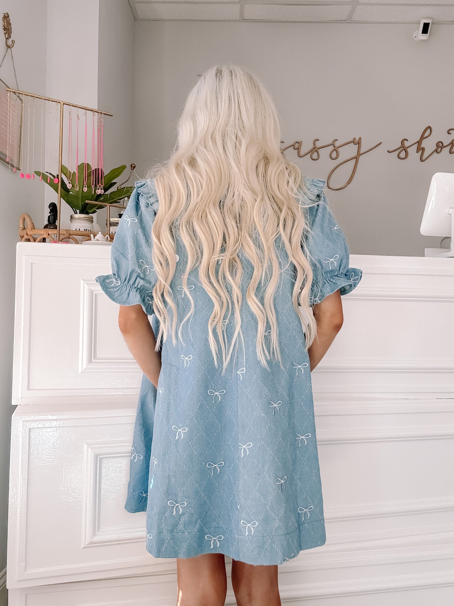 Light blue denim dress with embroidered white bows, puff sleeves, and a relaxed fit.