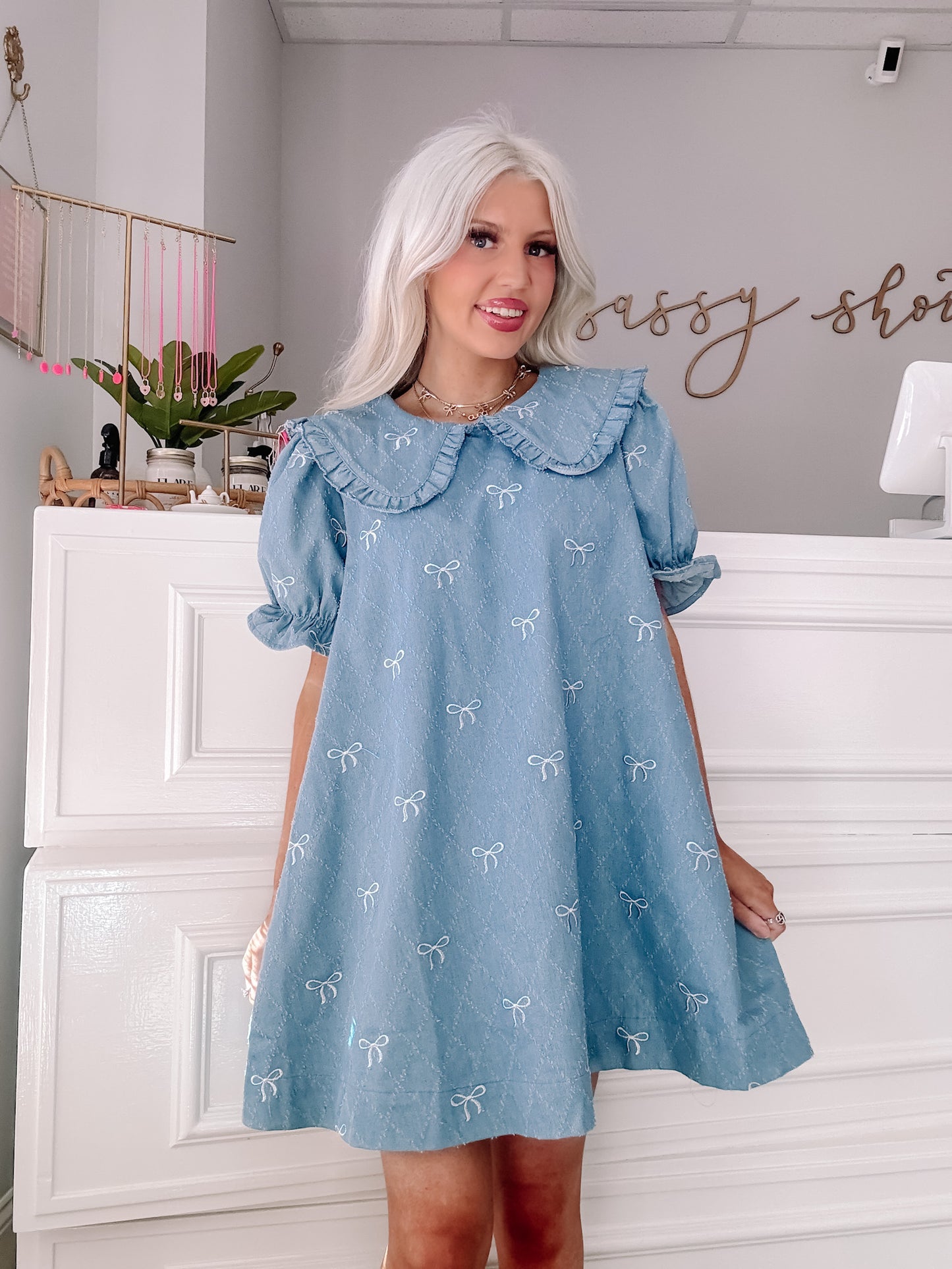 Light blue denim mini dress with embroidered white bows, peter pan collar, and short puff sleeves.