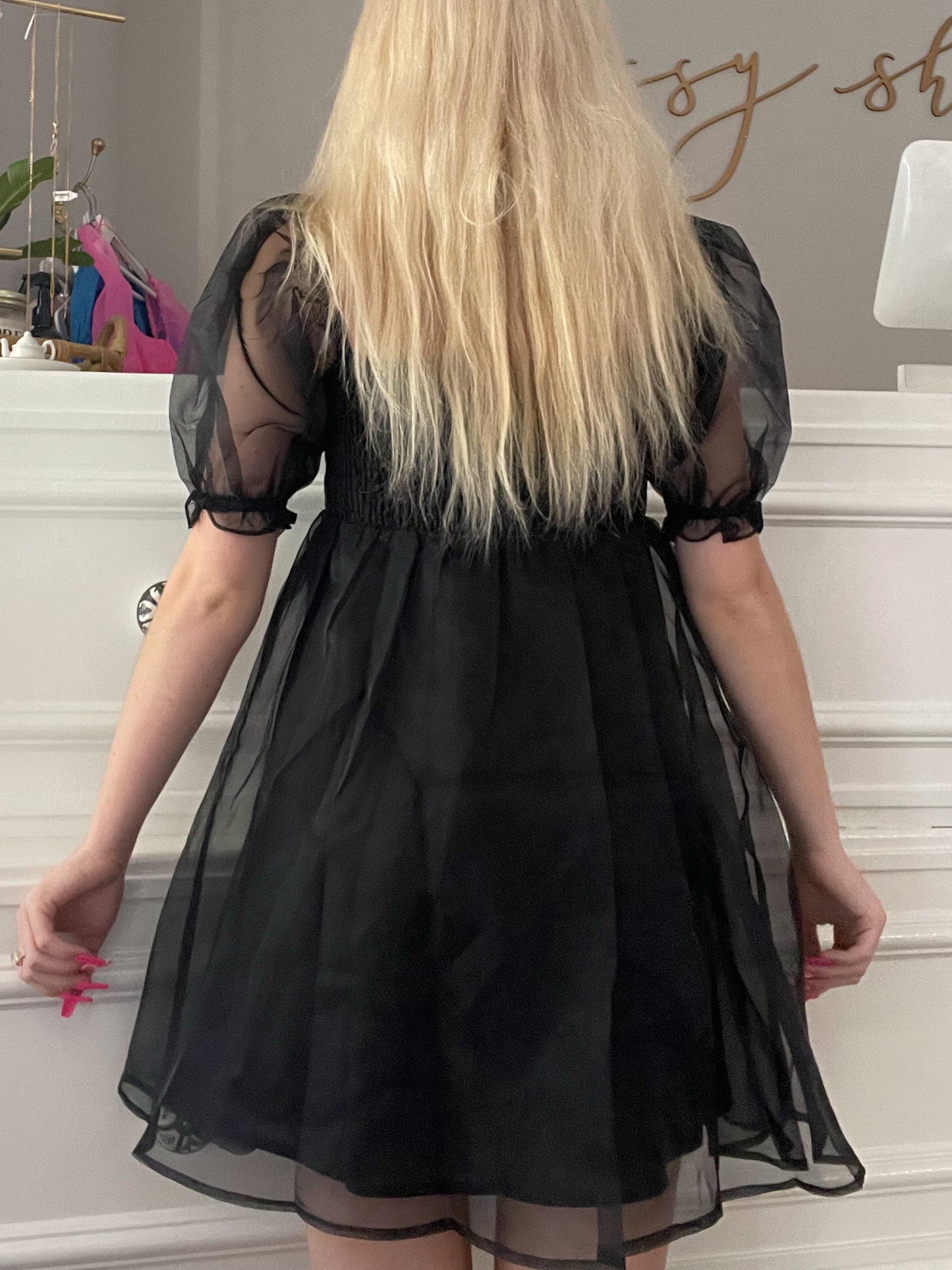 Black sheer organza mini dress with puff sleeves, shown from the back in a boutique setting.