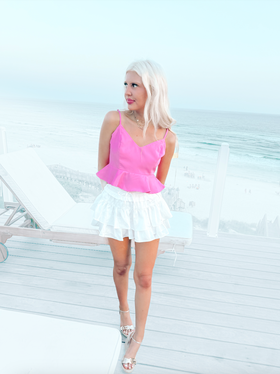 Pink satin camisole top paired with a white ruffled mini skirt, ocean view backdrop.