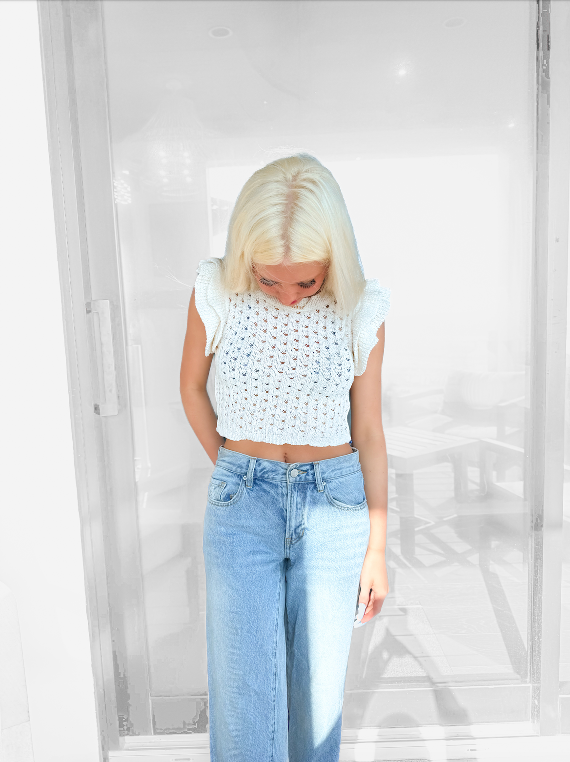 White open-knit cropped top with ruffle sleeves, modeled against a blurred background.
