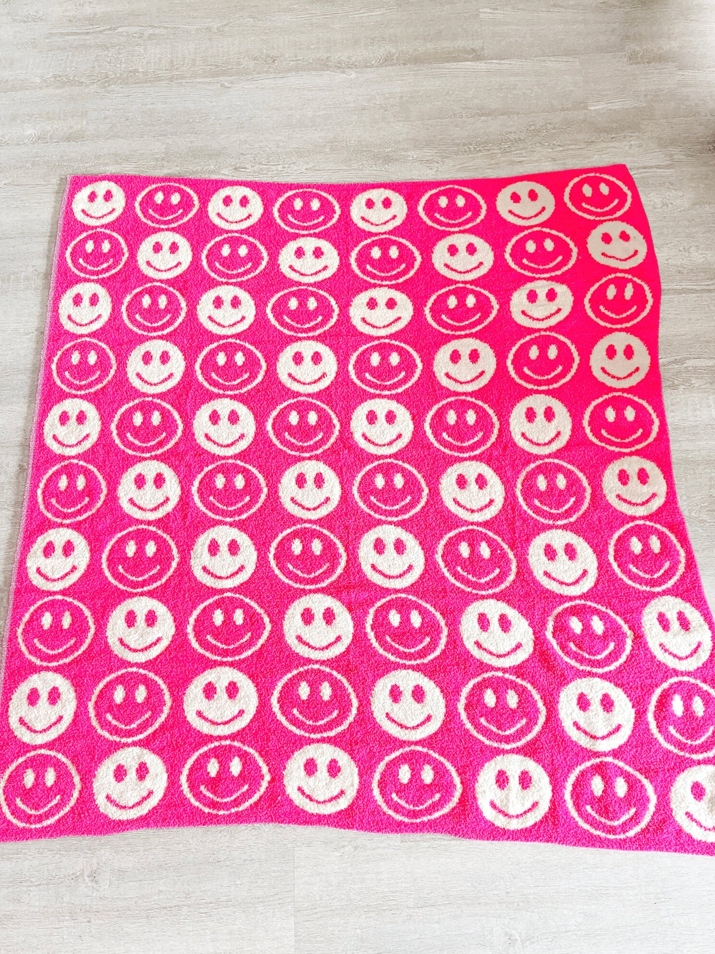 Pink fuzzy blanket with repeating smiling face pattern.