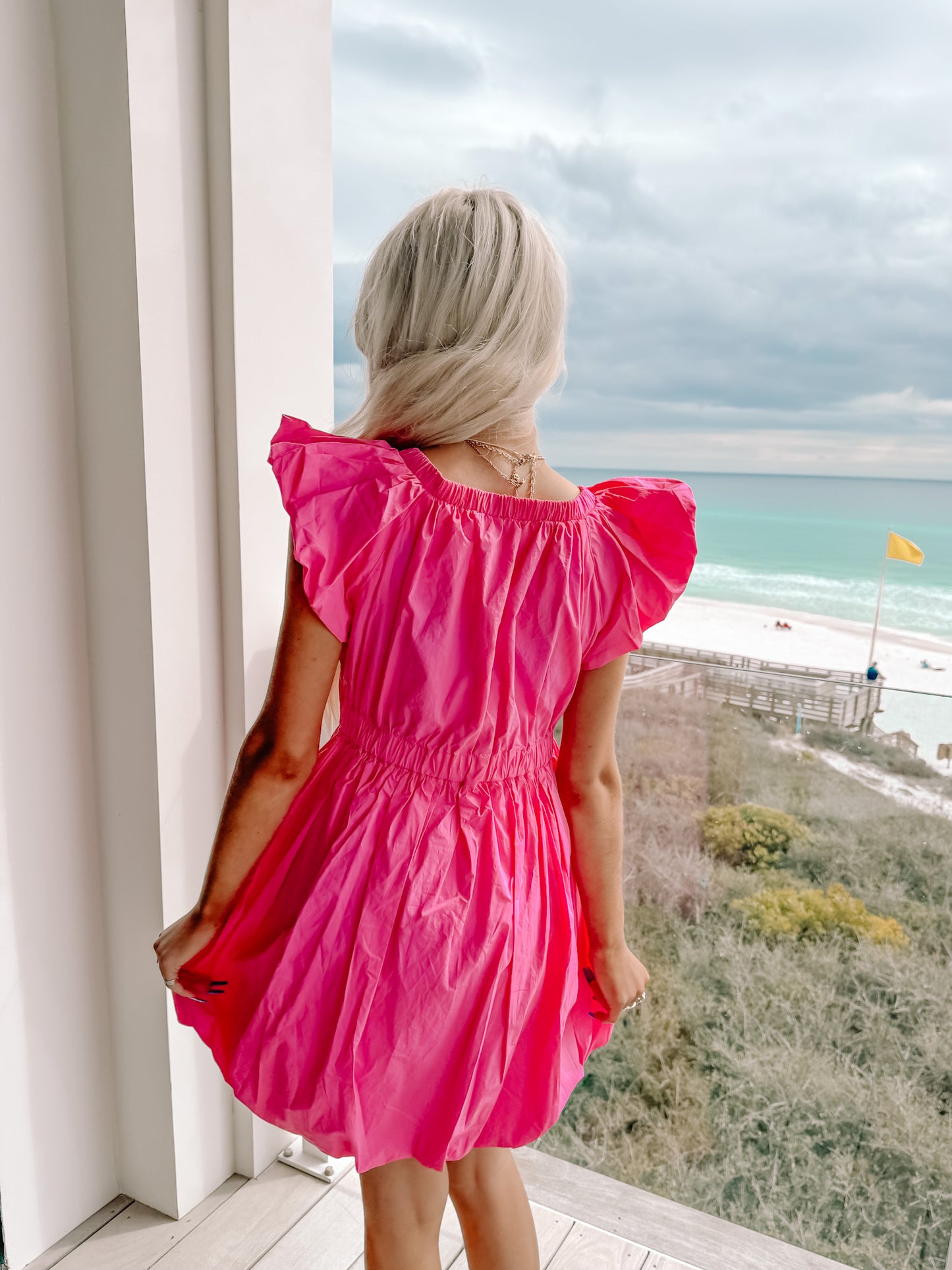 Hot pink mini dress with puff sleeves, viewed from behind overlooking the ocean.
