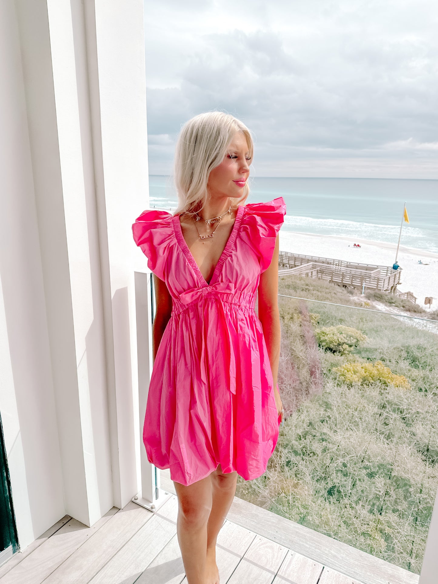 Hot pink bubble dress with ruffle sleeves, worn on a balcony overlooking the ocean.