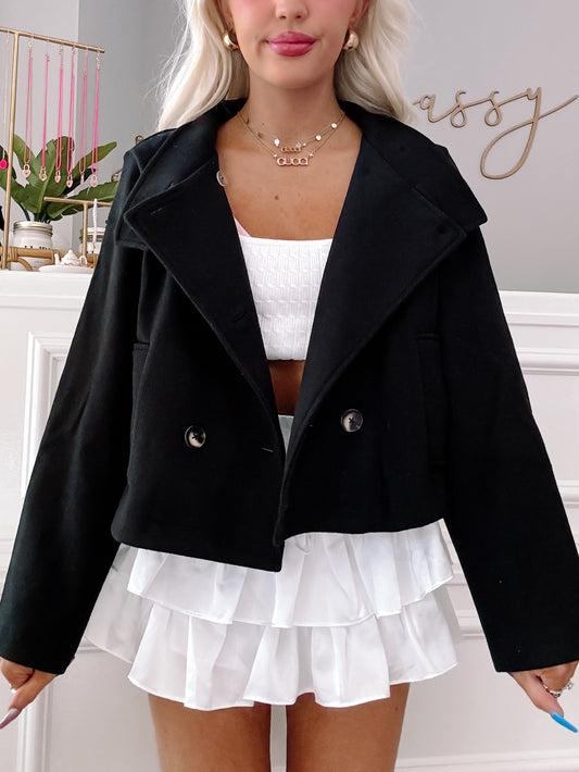 Black double-breasted cropped jacket styled over a white ruffled mini skirt.