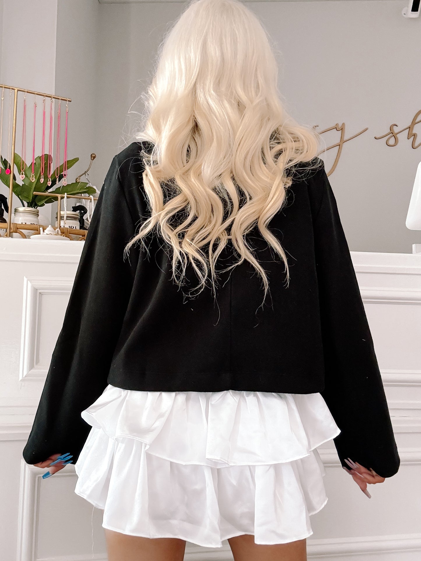 Black cropped jacket with a white ruffled trim, shown from the back in a shop setting.