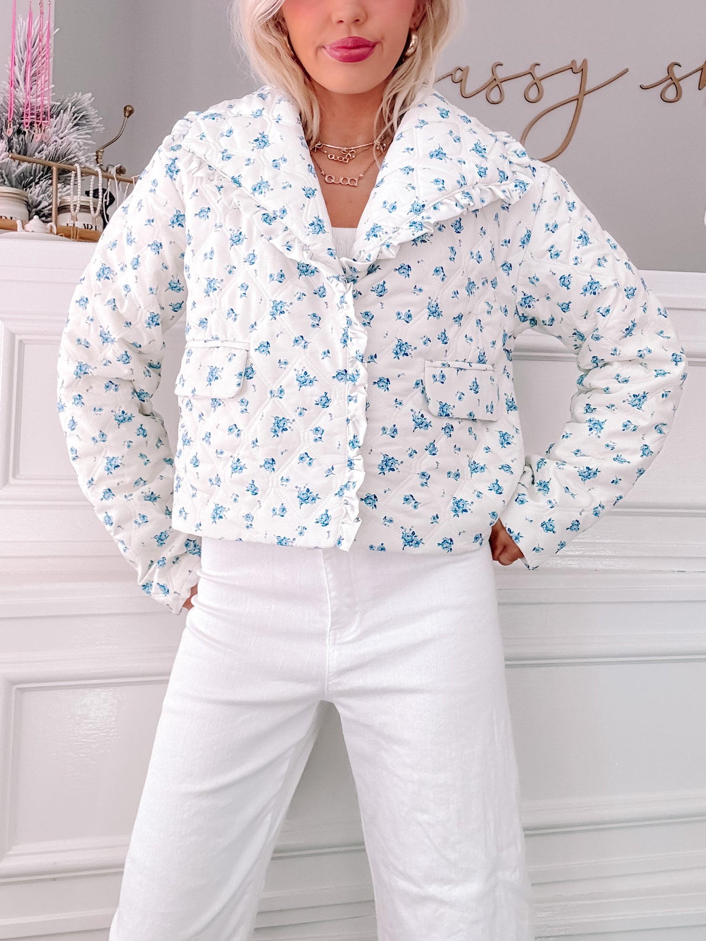 White quilted jacket with a blue floral print, ruffled collar, and front pockets.