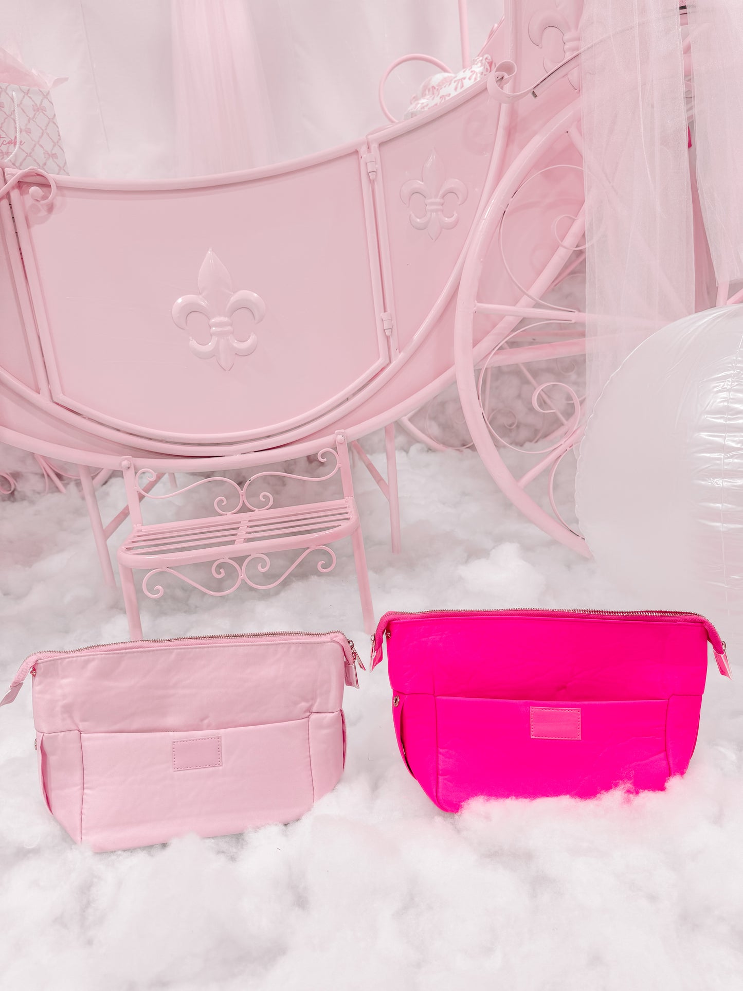 Pink and neon pink zippered pouches on fluffy white surface near pastel carriage.