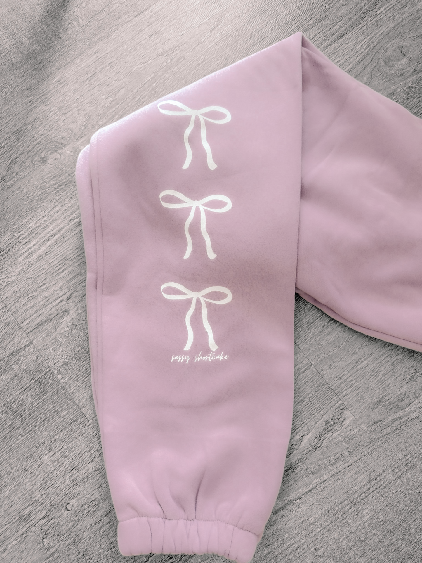 Lavender sweatpants with white bow accents, comfy fabric.