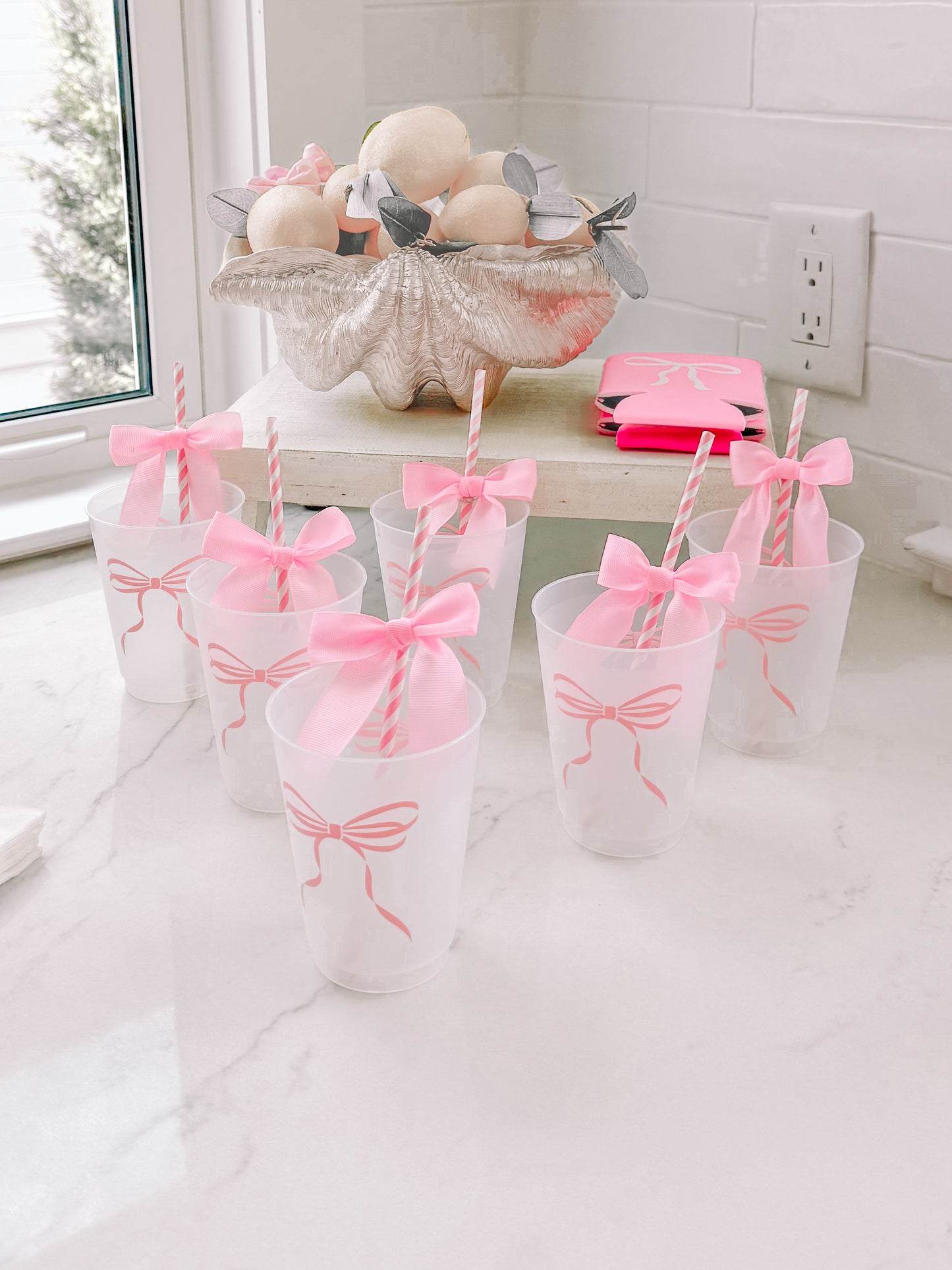 Pink bow-adorned cups on a marble counter, styled with striped straws.