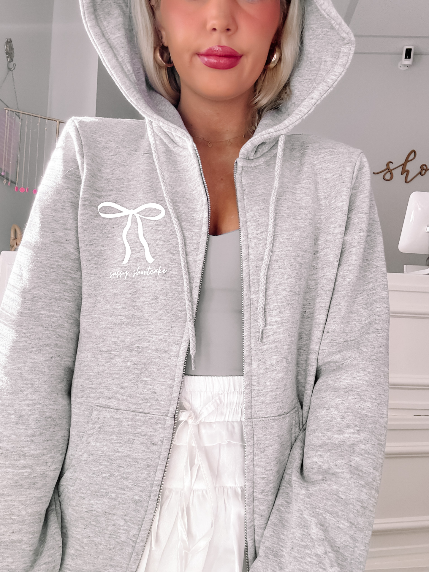 Grey zip-up hoodie featuring a bow and text detail, shown on a model.