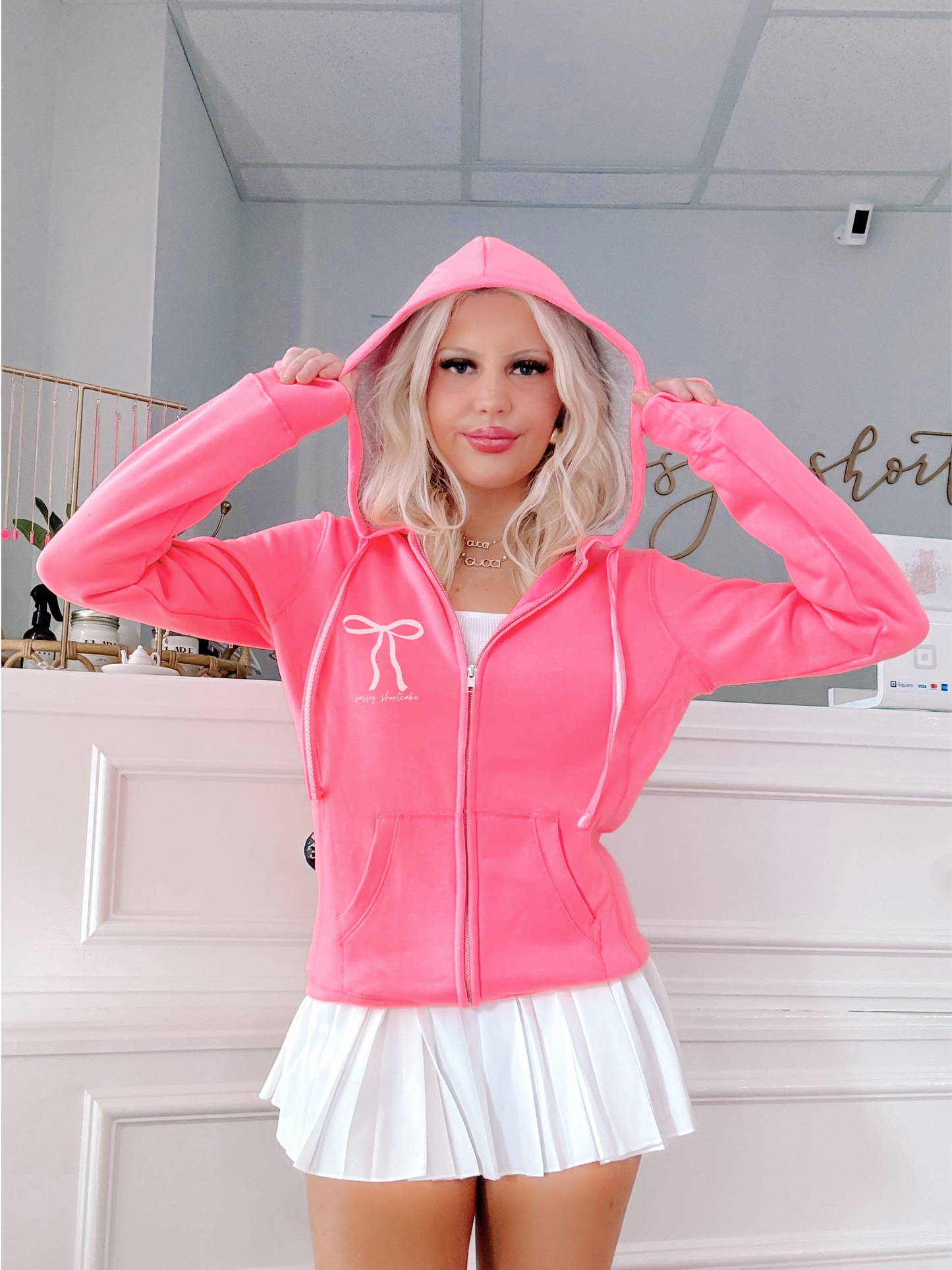 Neon pink zip-up hoodie with bow detail, modeled against a white wall.