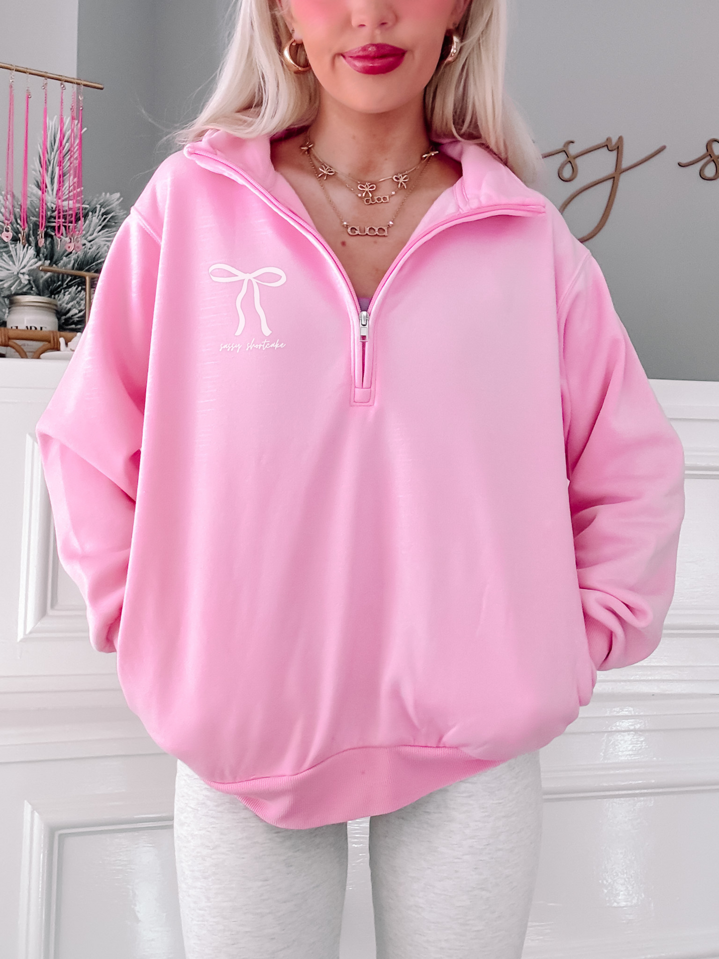 Pink quarter-zip sweatshirt with bow detail, modeled against a white wall.