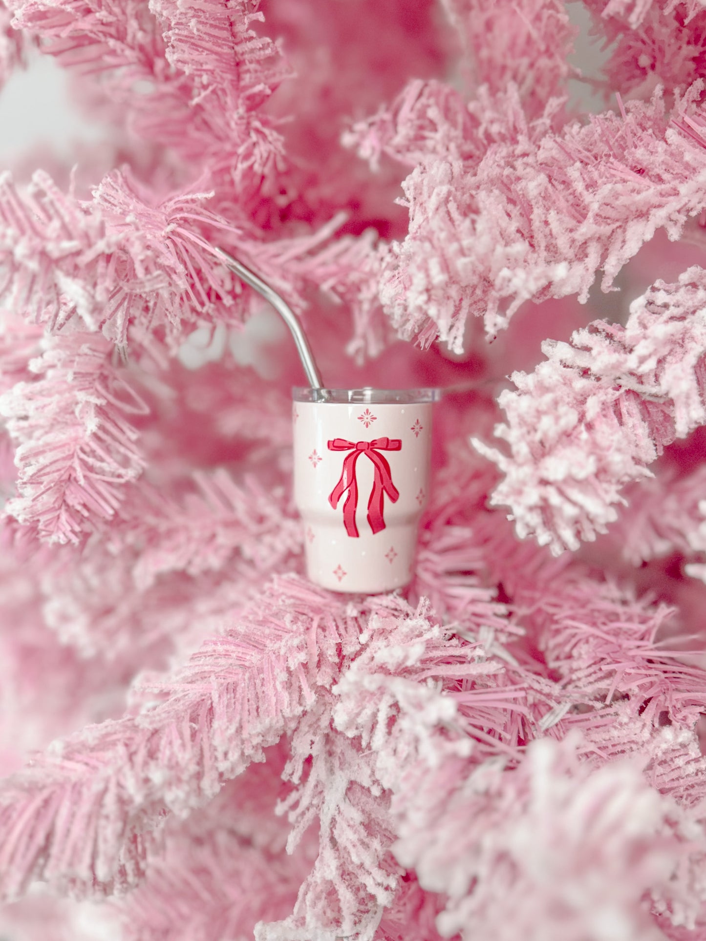 Pink tumbler with bow design nestled in a fluffy pink tree.