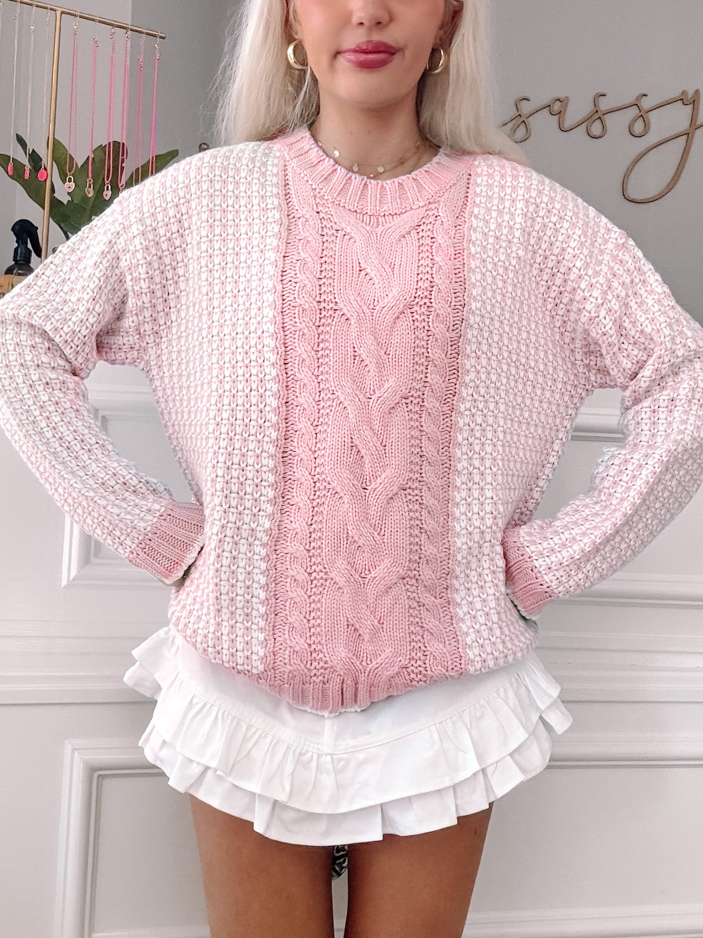 Pink and white cable-knit sweater with textured detailing, styled with a ruffled white skirt.