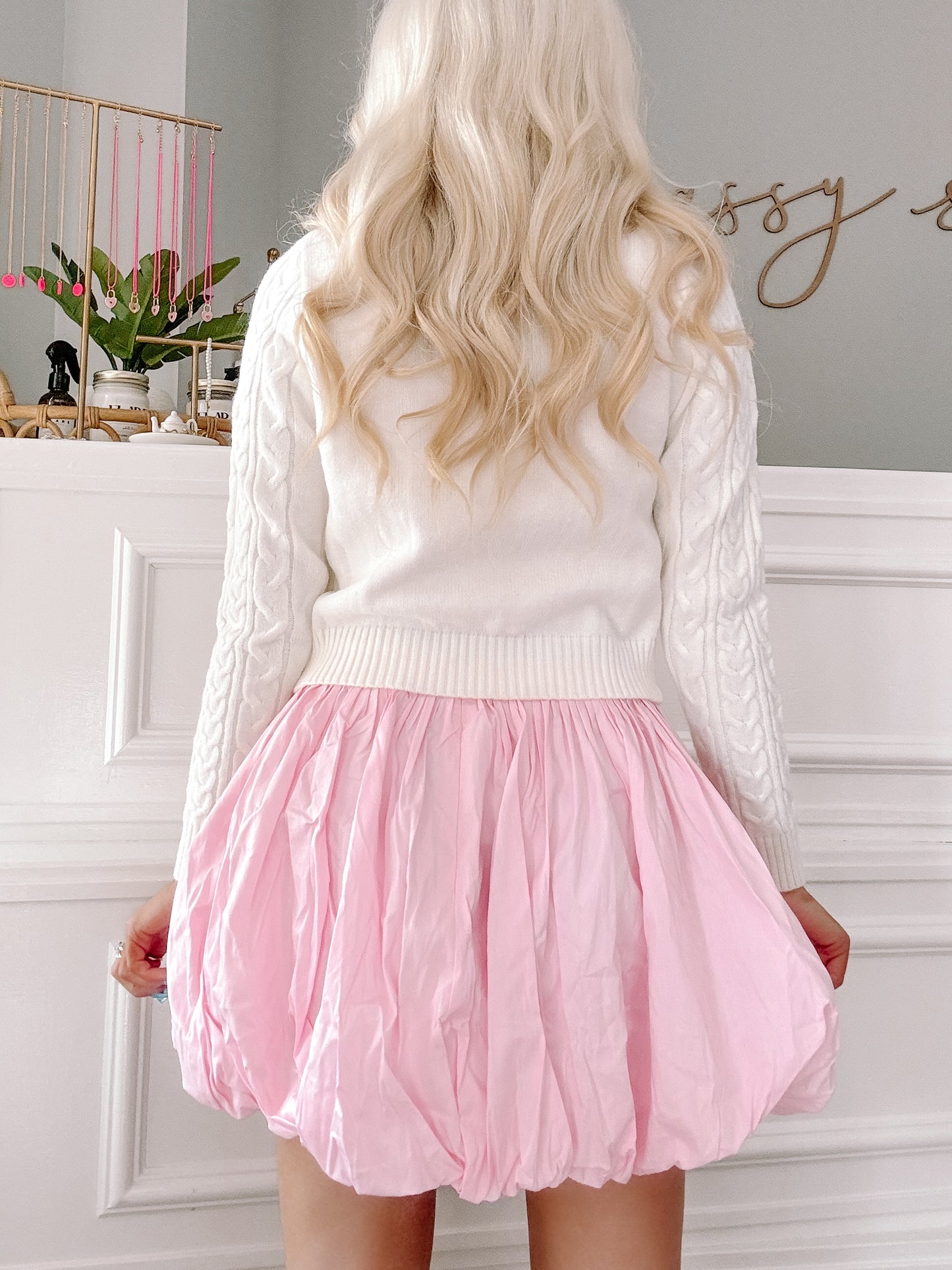 Pink bubble skirt styled with a white cable knit sweater against a white wall.
