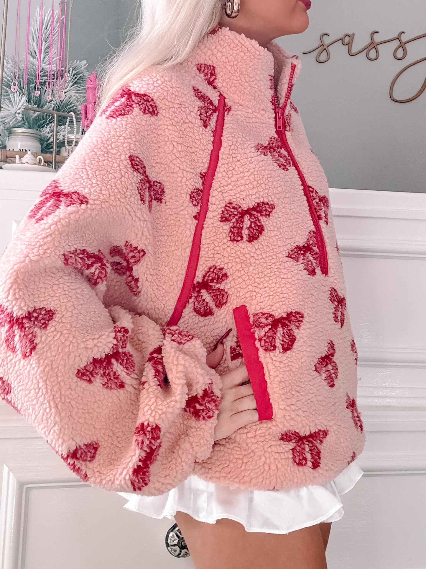 Pink sherpa pullover with red bow pattern, half-zip closure.