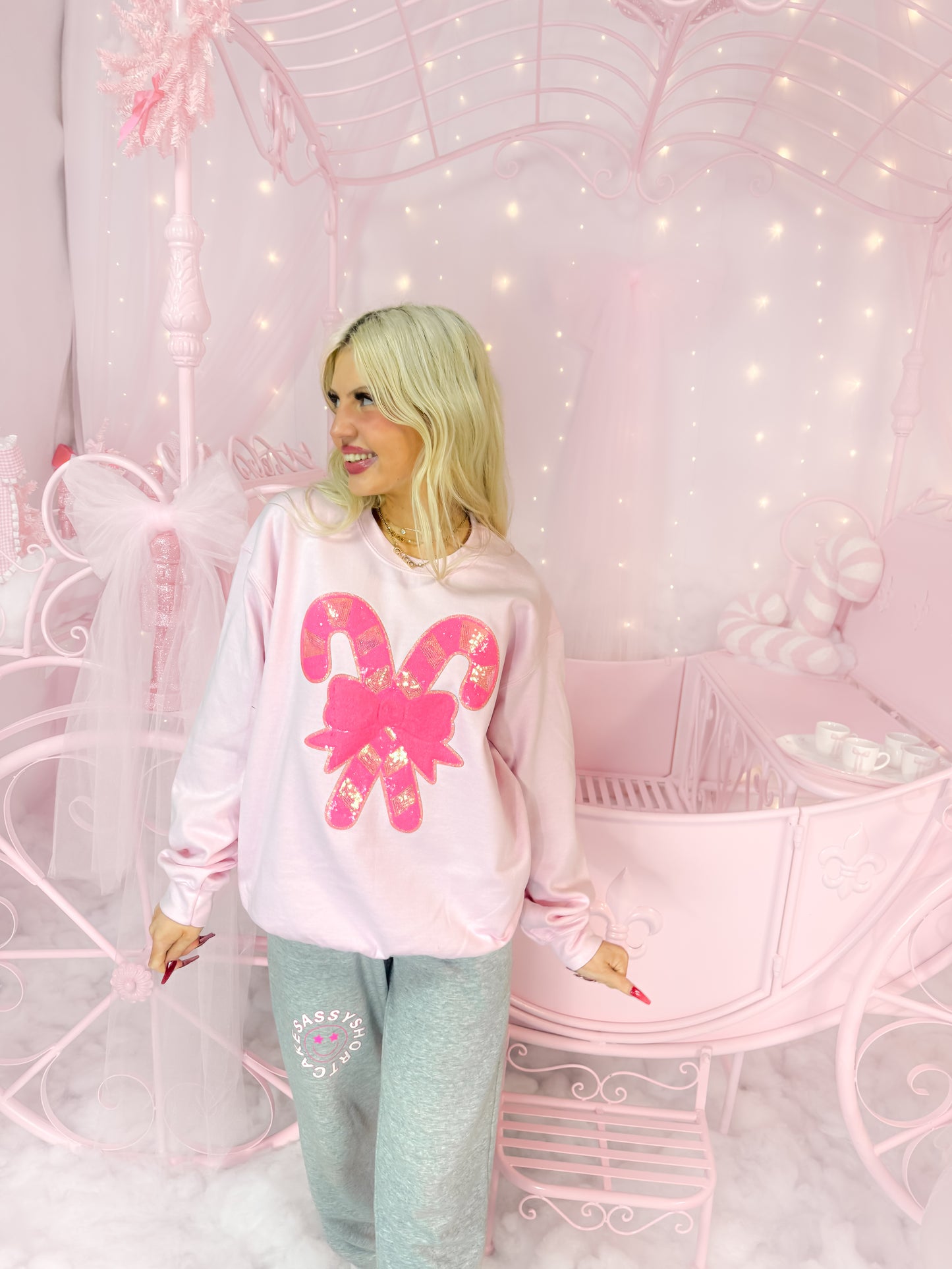 Pink candy cane sweatshirt with sequined detail, modeled in a whimsical pink setting.