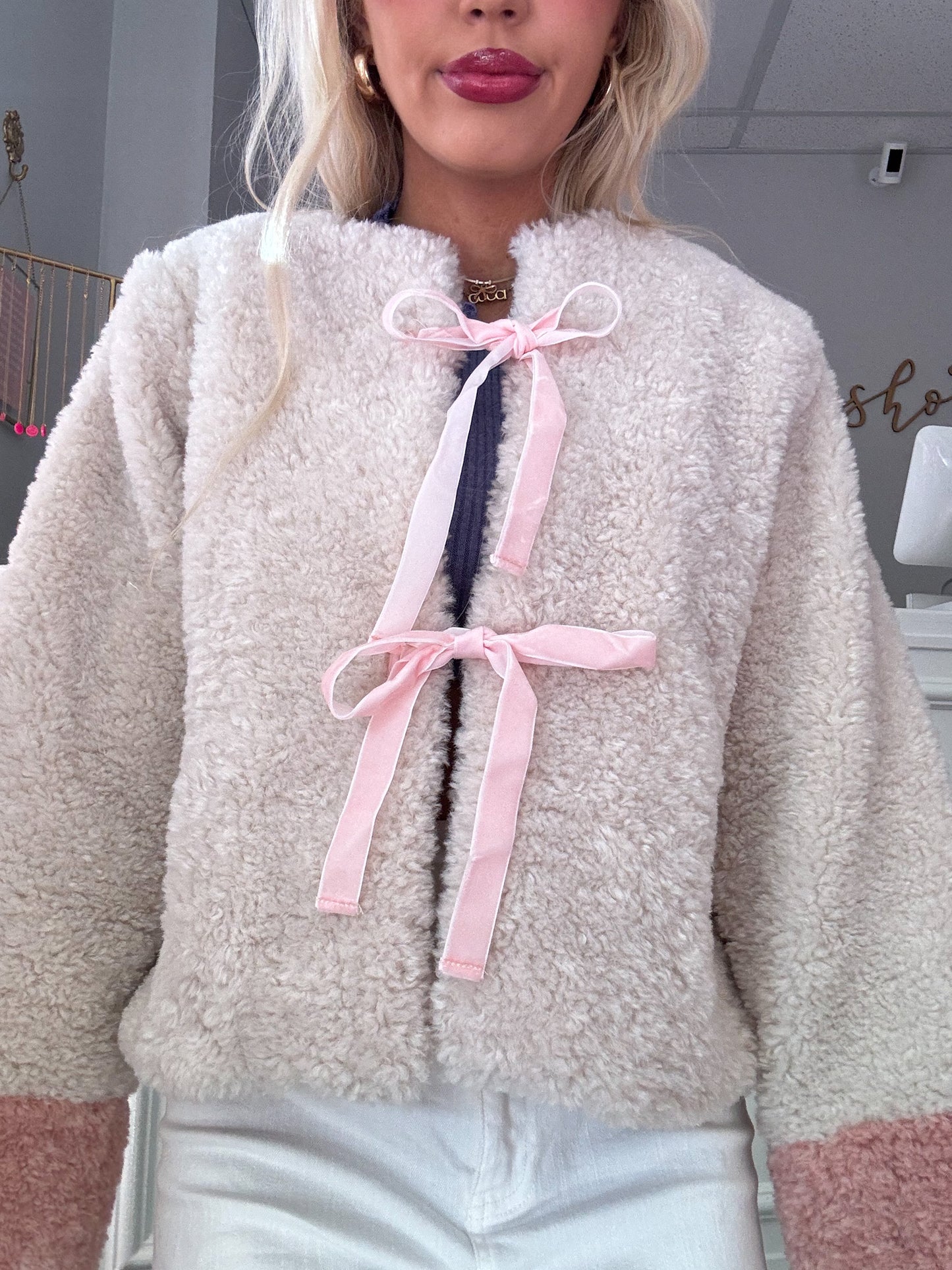 Cream-colored sherpa jacket with pink ribbon detailing, cozy and soft texture.