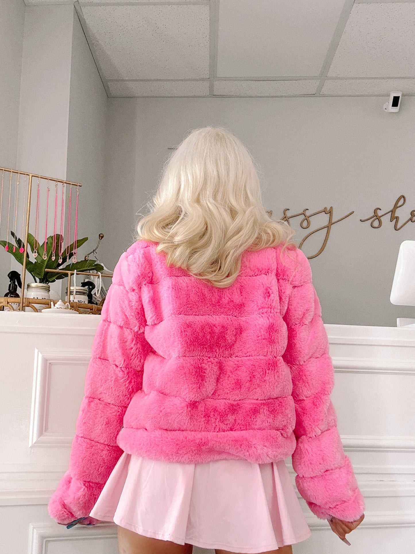 Hot pink fluffy faux fur coat, shown from the back in a bright interior setting.