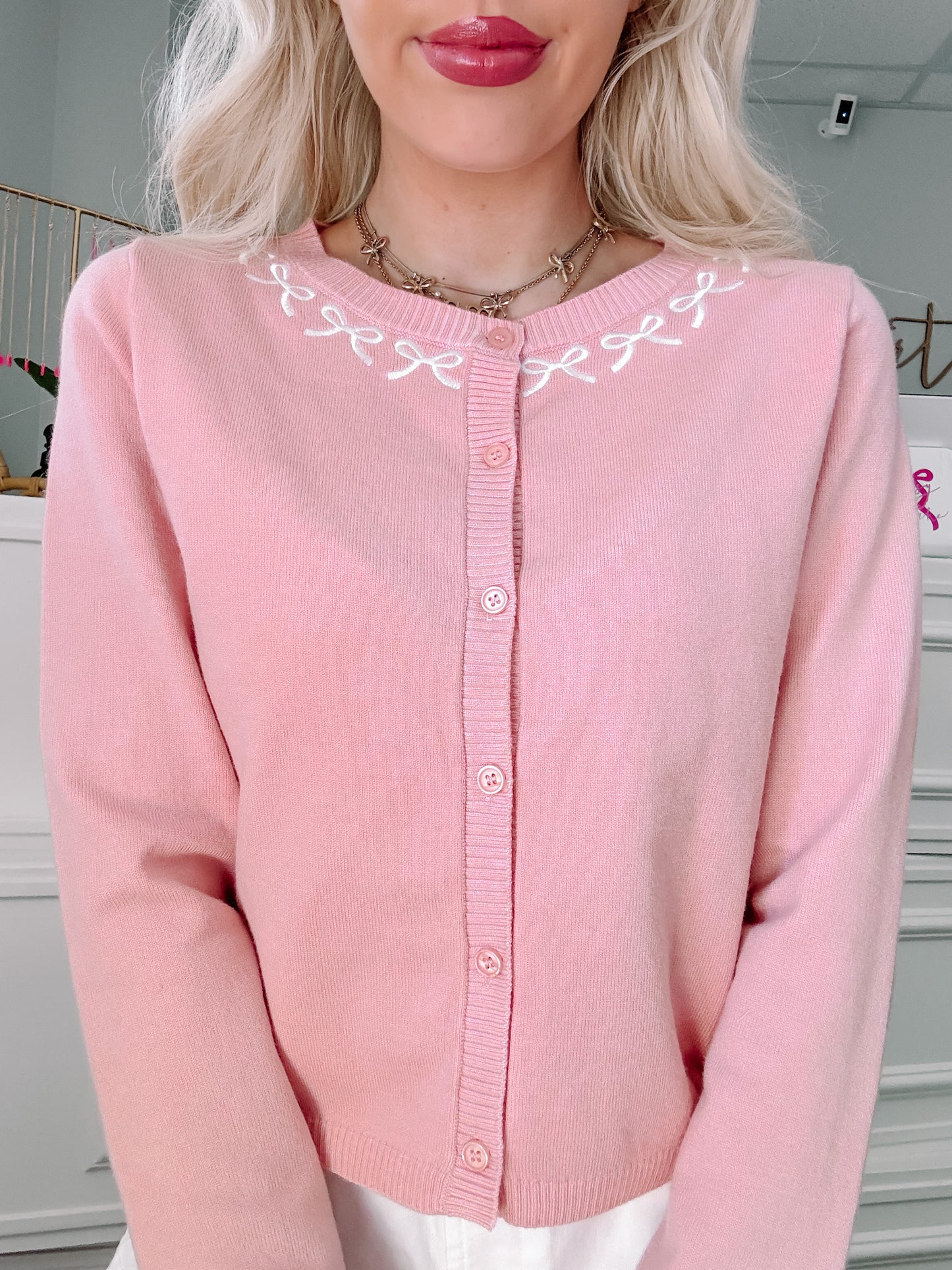 Pink button cardigan with embroidered bow detail.