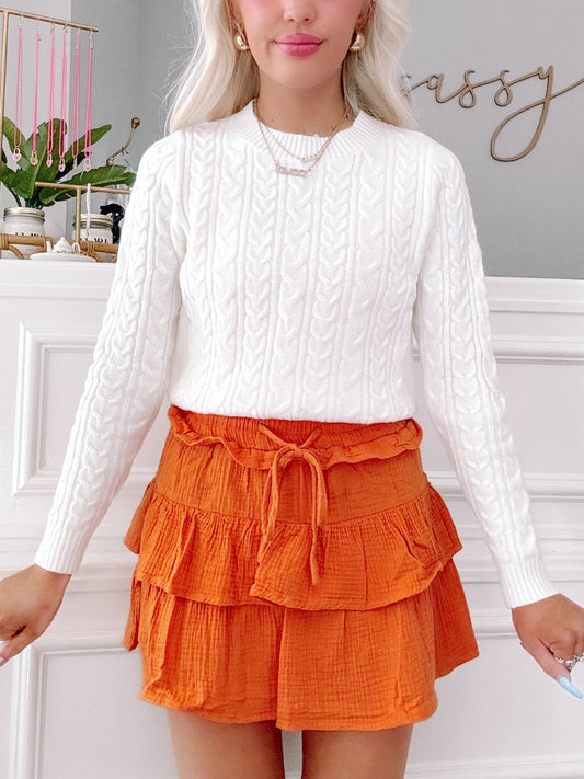 Tiered orange linen mini skirt with drawstring waist, paired with a white cable knit sweater. Flirtatious Orange linen ruffle mini skirt from Sassy Shortcake