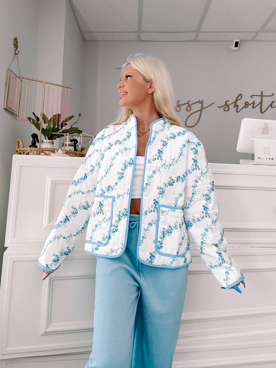 Blue floral quilted jacket with light blue trim, modeled against a white background.