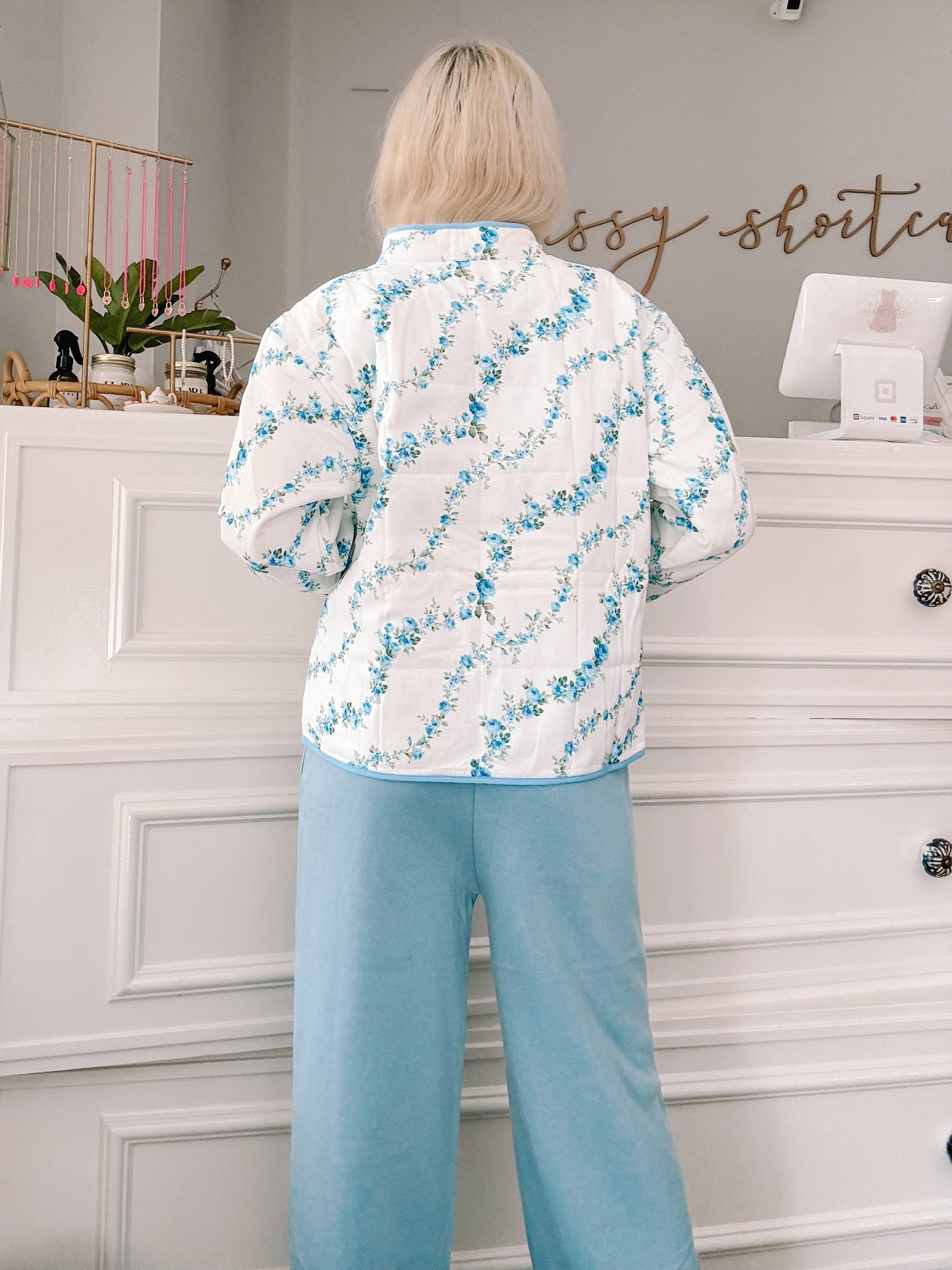 Blue floral quilted jacket, rear view, light blue pants.