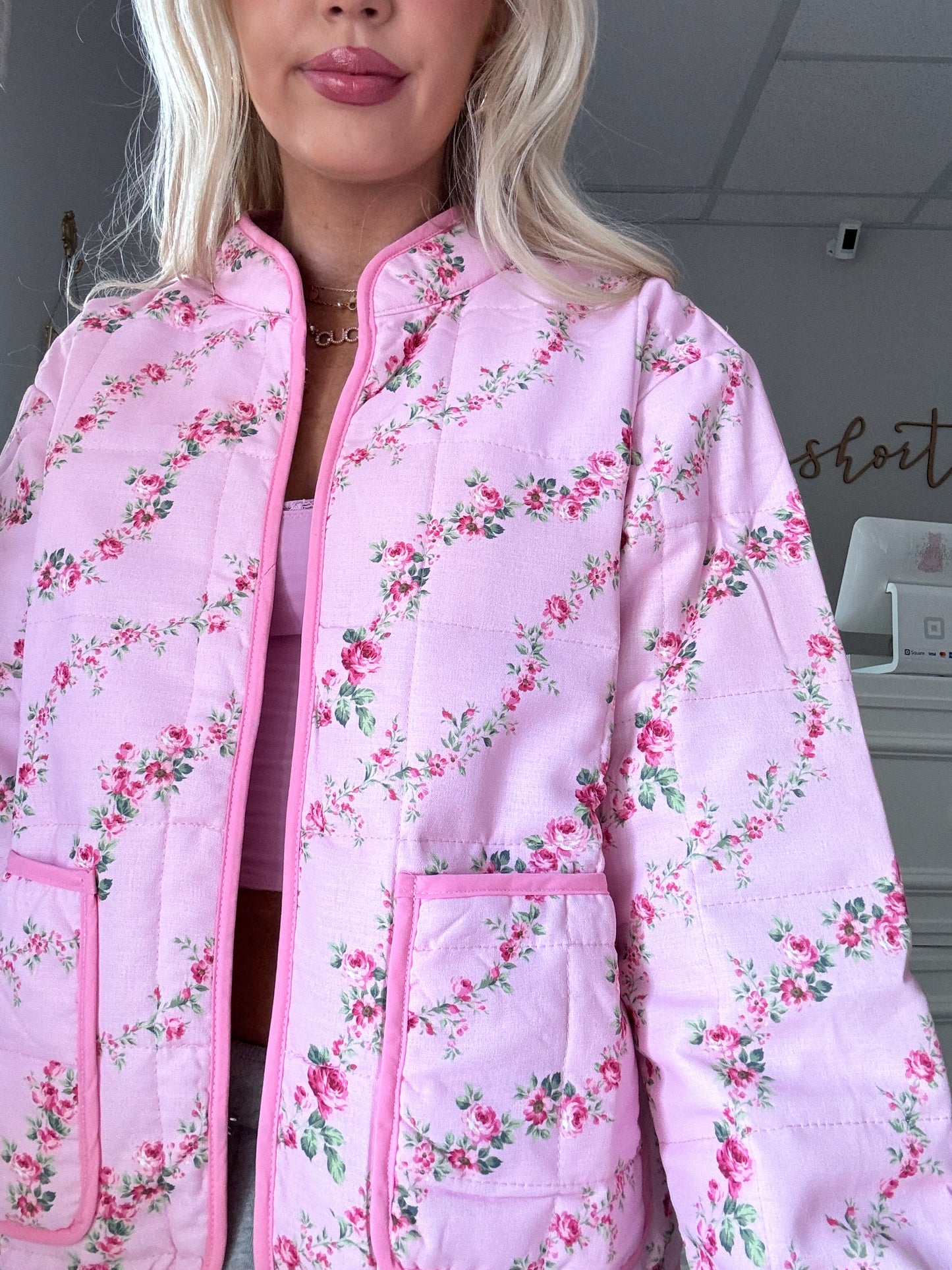 Pink quilted jacket with a delicate floral pattern, featuring patch pockets.