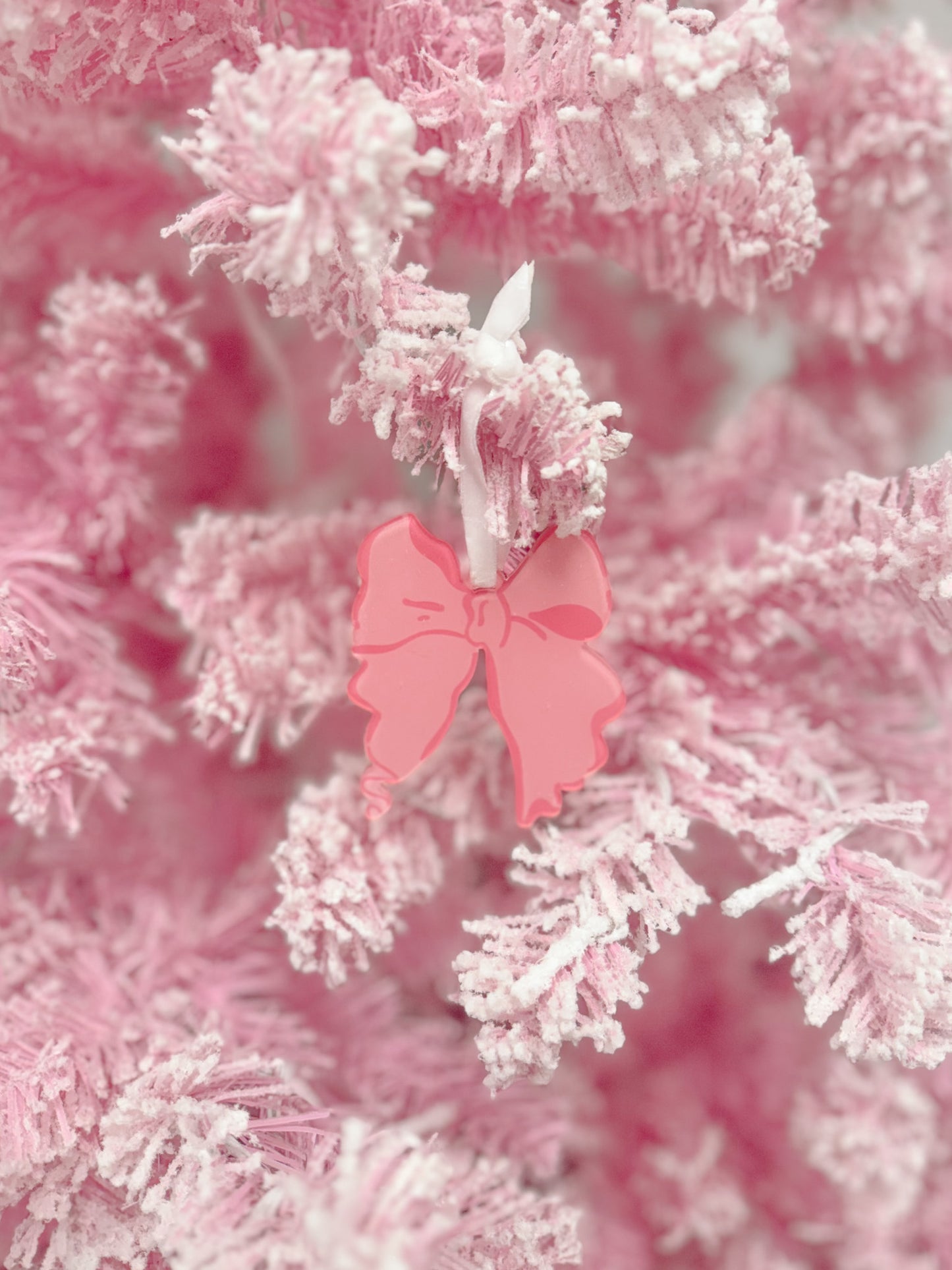 Pink bow ornament hanging on a flocked pink Christmas tree.
