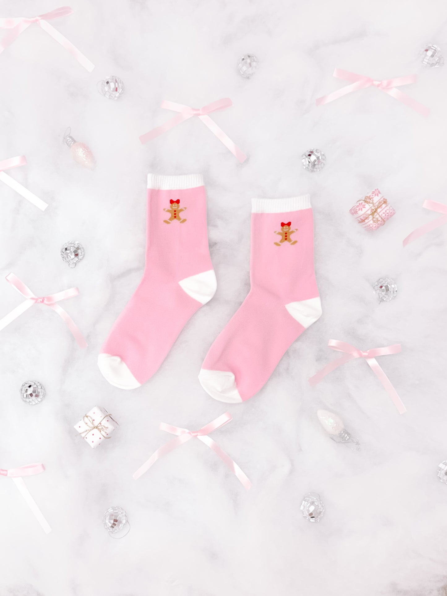 Pink socks with gingerbread man design, arranged on marble with festive decor.
