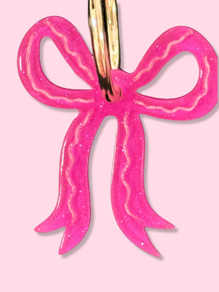 Pink glitter bow earrings with gold hoops; close-up view.