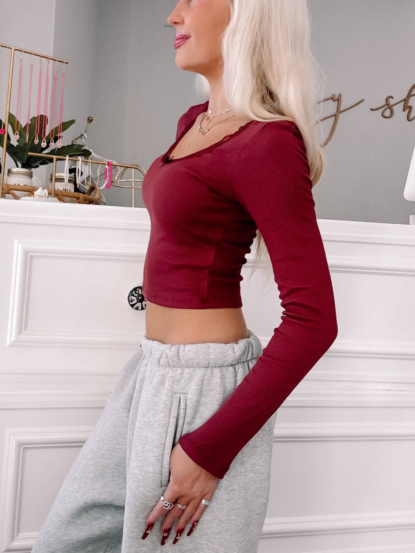Burgundy long-sleeve fitted top with lace trim, modeled against a white wall.
