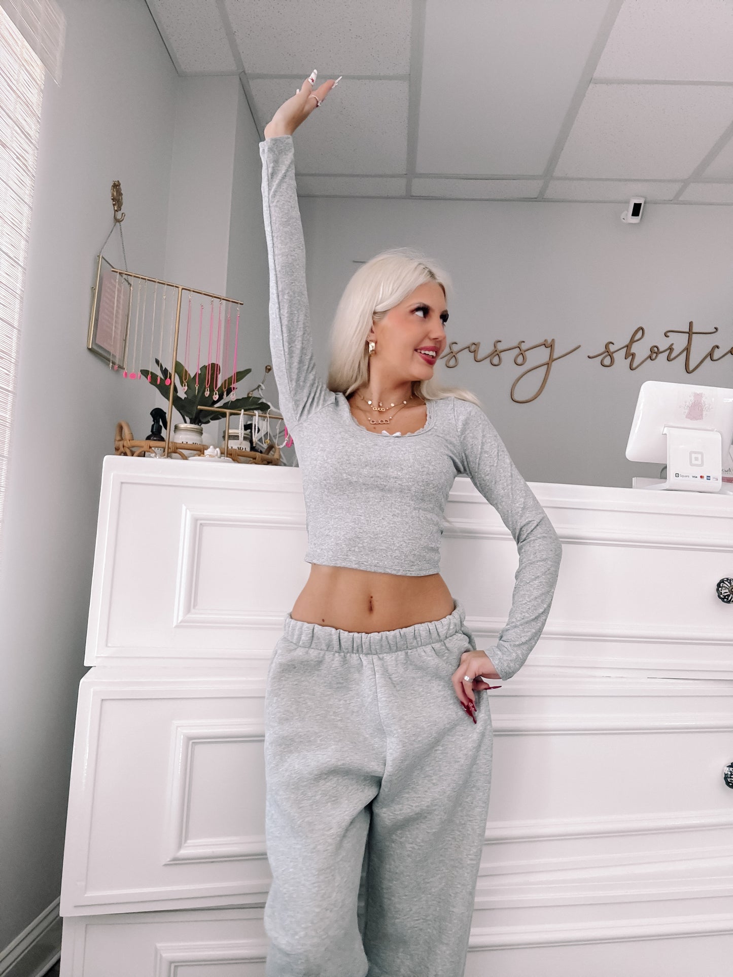 Grey long-sleeve crop top and sweatpants outfit; model poses in a boutique.