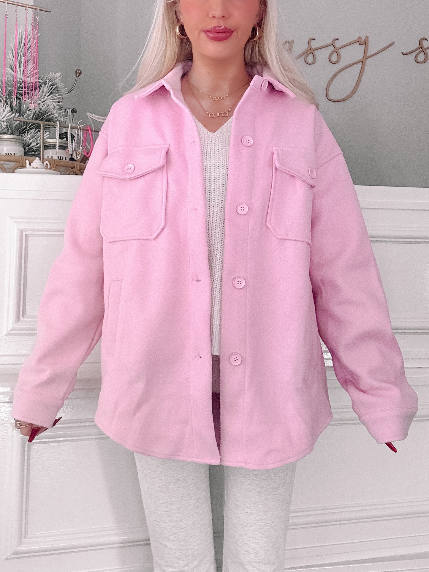 Pink shacket with button closure, modeled indoors against a white paneled wall.