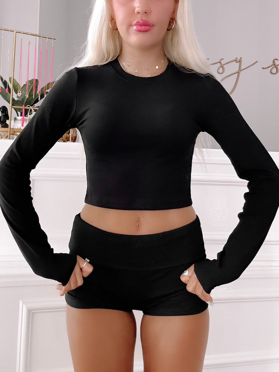 Black long-sleeve crop top and shorts set, shown on a model against a white wall.