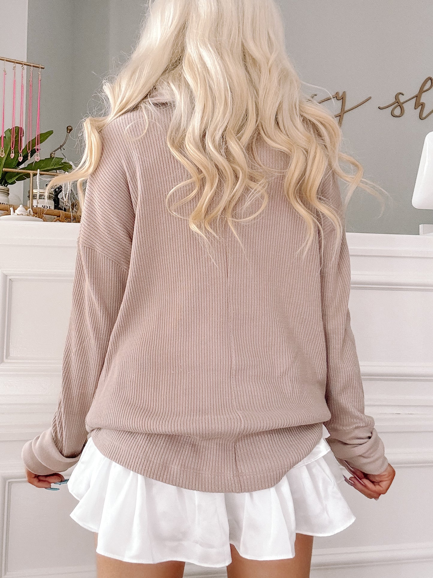 Taupe ribbed knit pullover with long sleeves, paired with a white ruffled mini skirt.